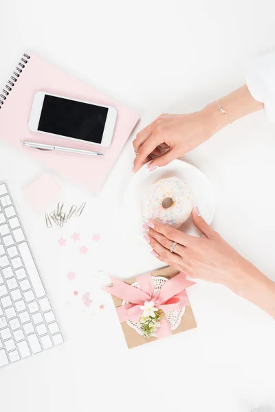 Female hands with donut at workplace — Stock Photo