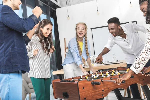 Colegas multiculturales jugando al futbolín - foto de stock