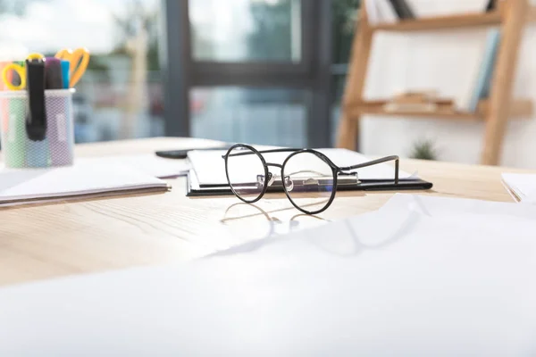 Eyeglasses on workplace with papers — Stock Photo