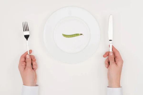 Manos, cubiertos y guisantes en el plato - foto de stock