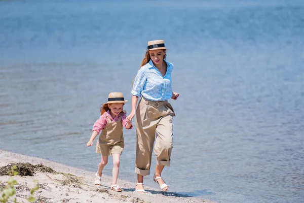 Madre e hija caminando a la orilla del mar - foto de stock