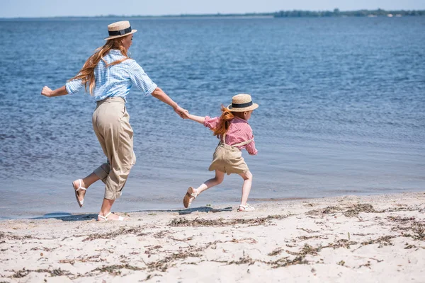 Madre e hija caminando a la orilla del mar - foto de stock