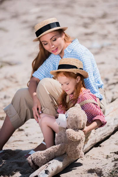 Mother and daughter with teddy bear on beach — Stock Photo