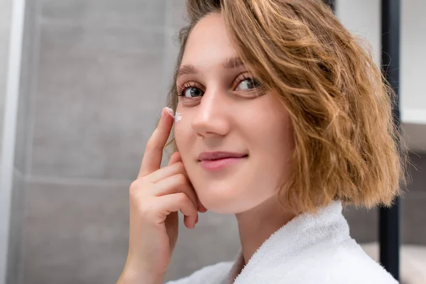 Mujer aplicando crema facial - foto de stock