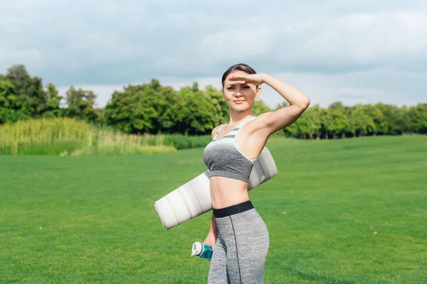 Woman holding water bottle and yoga mat — Stock Photo