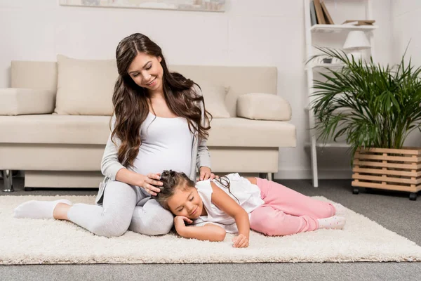 Беременная женщина с дочерью, сидящей на ковре — стоковое фото