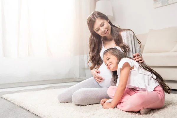 Mujer embarazada con hija escuchando el vientre - foto de stock