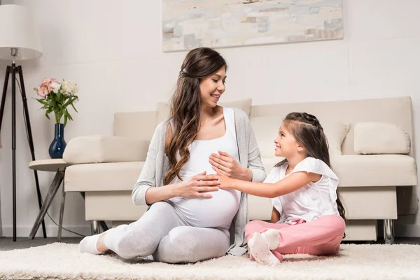 Pregnant woman with daughter touching belly — Stock Photo