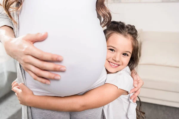 Chica abrazando embarazada madre - foto de stock