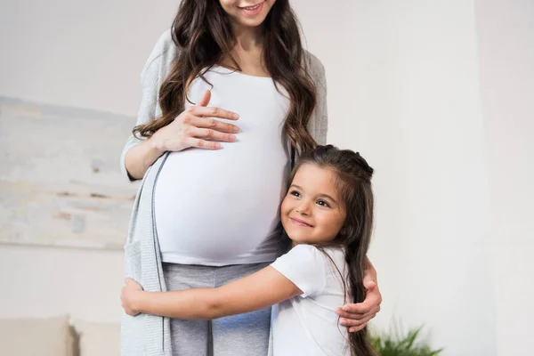 Chica abrazando embarazada madre - foto de stock