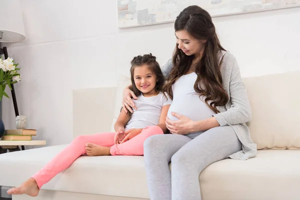 Pregnant woman hugging daughter on couch — Stock Photo