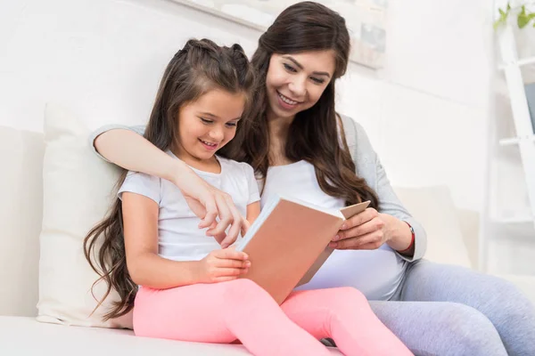 Niña leyendo libro con madre - foto de stock