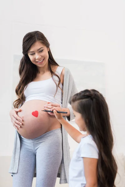 Girl drawing on pregnant belly of mother — Stock Photo
