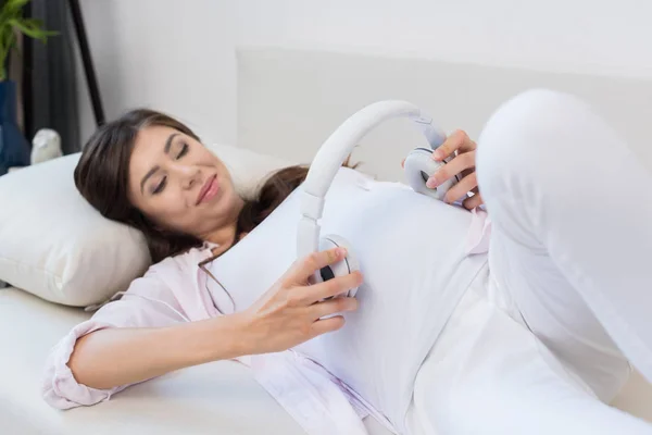 Femme enceinte tenant des écouteurs — Photo de stock