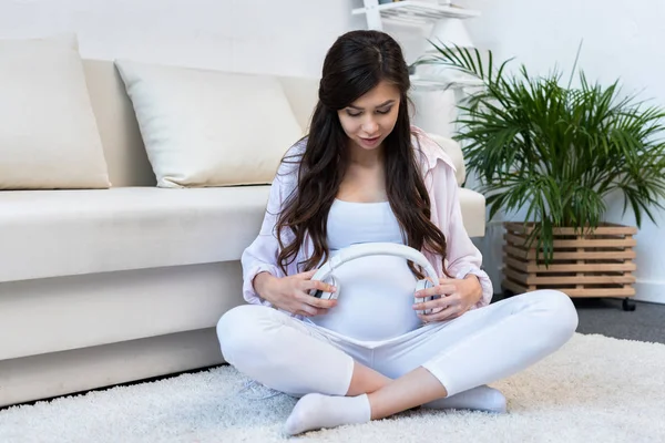 Mujer embarazada sosteniendo auriculares sobre el vientre - foto de stock