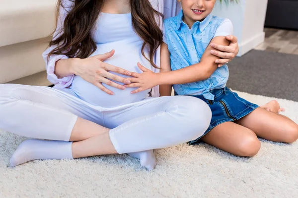 Беременная женщина с дочерью трогает живот — стоковое фото
