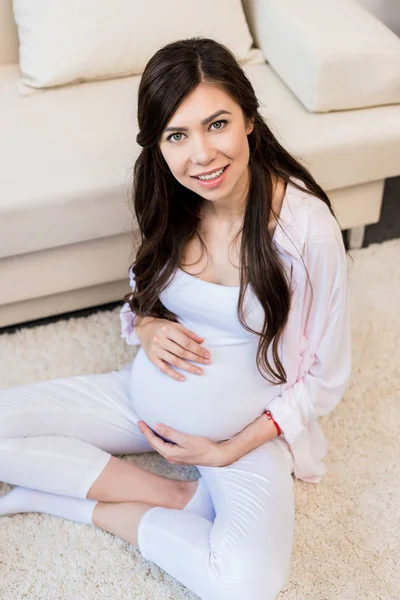 Беременная женщина сидит на полу — стоковое фото