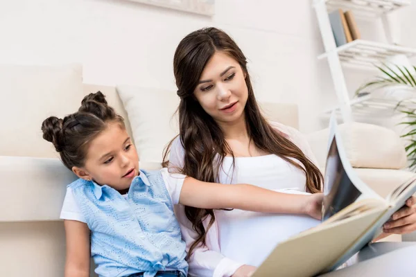 Girl and pregnant mother reading book — Stock Photo