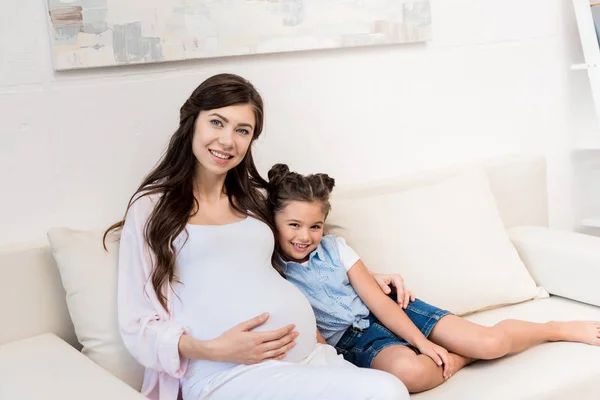 Chica y madre embarazada abrazándose en el sofá - foto de stock