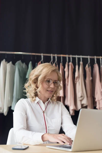 Donna d'affari che utilizza il computer portatile nel negozio di abbigliamento — Foto stock