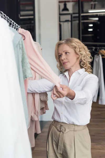 Mujer eligiendo ropa en tienda de ropa - foto de stock