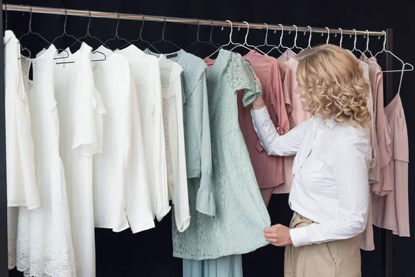 Mujer eligiendo ropa en tienda de ropa - foto de stock