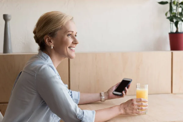 Жінка зі смартфоном п'є сік — стокове фото
