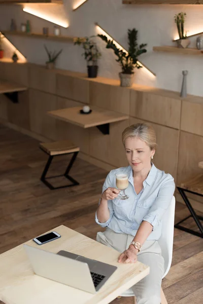 Femme buvant du café et utilisant un ordinateur portable — Photo de stock