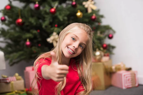 Child with thumb up at christmas tree — Stock Photo