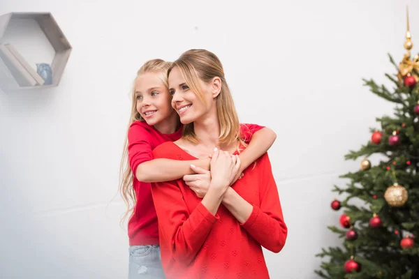 Madre e hija abrazándose en el árbol de Navidad - foto de stock