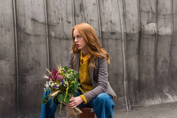 Girl with bouquet sitting on suitcase — Stock Photo