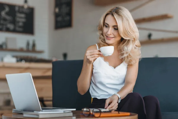 Жінка п'є каву і використовує ноутбук — стокове фото