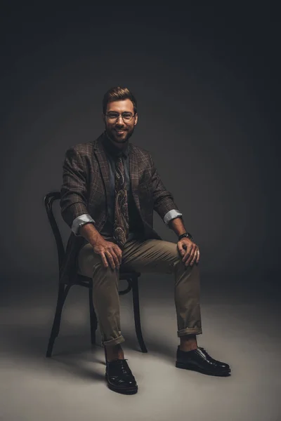 Homme souriant en costume assis sur une chaise — Photo de stock