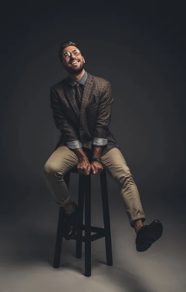 Riendo hombre de traje sentado en el taburete - foto de stock