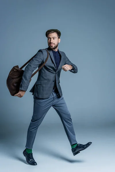 Young man in suit and flat cap, walking with leather bag on his shoulder — Stock Photo