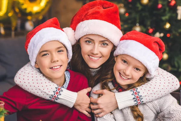 Mamma che abbraccia con i bambini in cappelli da Babbo Natale — Foto stock