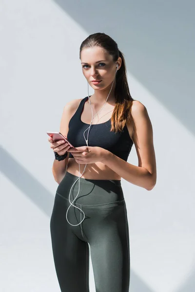Sportswoman in earphones using smartphone — Stock Photo