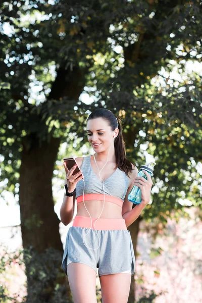 Sportswoman in earphones using smartphone — Stock Photo