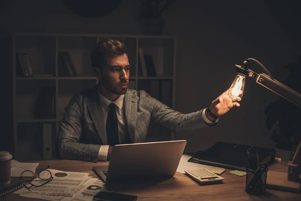 Empresário tocando lâmpada de mesa no local de trabalho — Fotografia de Stock