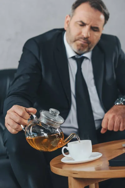 Hombre de negocios vertiendo té en la taza - foto de stock