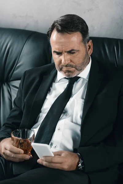 Бизнесмен со стаканом виски с помощью смартфона — стоковое фото