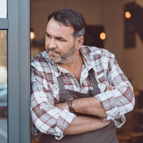 Bartender leaning on entrance of cafe — Stock Photo