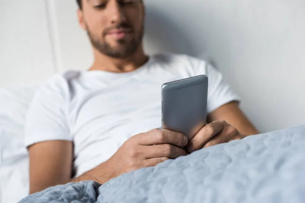 Man using smartphone in bed — Stock Photo