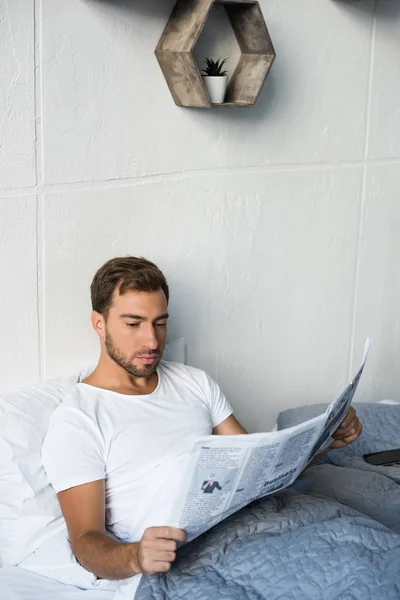 Man in bed reading newspaper — Stock Photo