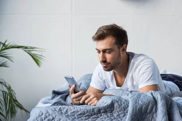 Человек в постели с помощью смартфона — стоковое фото