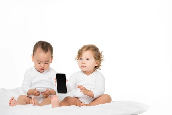 Niños pequeños multiculturales con teléfonos inteligentes digitales - foto de stock