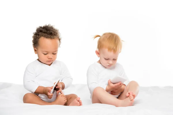 Niños pequeños multiculturales con teléfonos inteligentes digitales - foto de stock