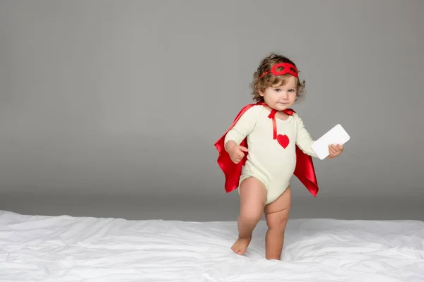 Toddler in superhero costume with smartphone — Stock Photo