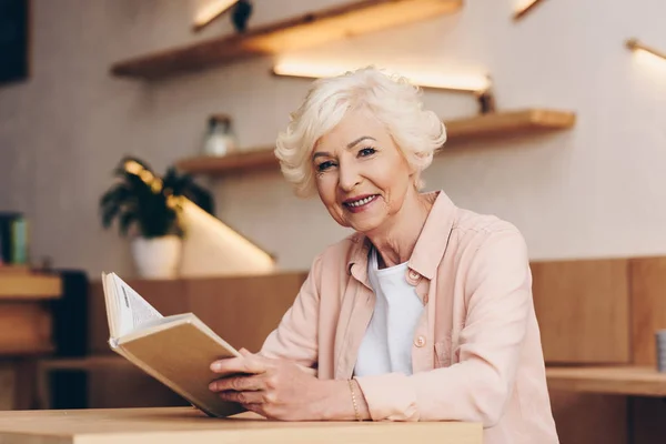 Femme âgée avec livre dans un café — Photo de stock