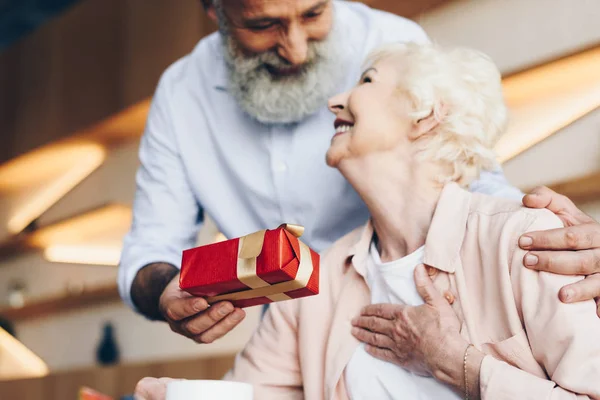 Senior man surprising wife with gift — Stock Photo